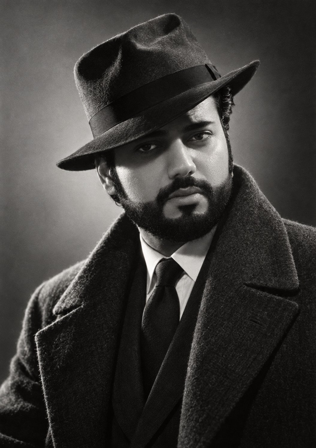 Manvedeep Singh in a fedora and overcoat, monochrome study